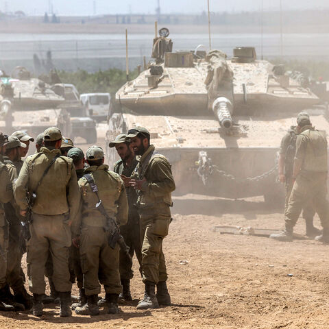 Israeli army soldiers huddle together before a main battle tank positioned in southern Israel near the border with the Gaza Strip on May 9, 2024, amid the ongoing conflict in the Palestinian territory between Israel and the Hamas movement. (Photo by AHMAD GHARABLI / AFP) (Photo by AHMAD GHARABLI/AFP via Getty Images)