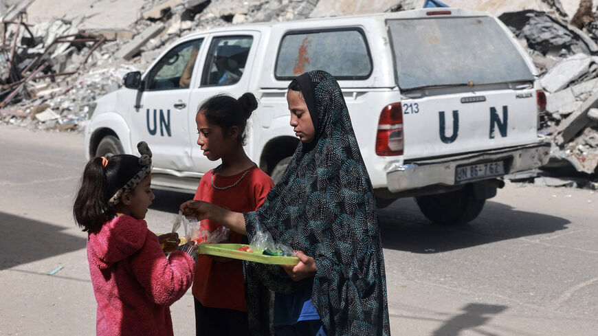 A United Nations vehicle drives by as Palestinian girls share a food ration in Rafah, amid the ongoing conflict between Israel and Hamas, Gaza Strip, March 31, 2024.