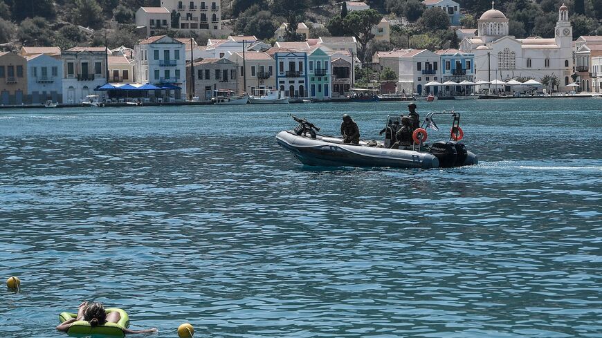 A woman enjoys the sea as a Greek army rib returns from patrol.