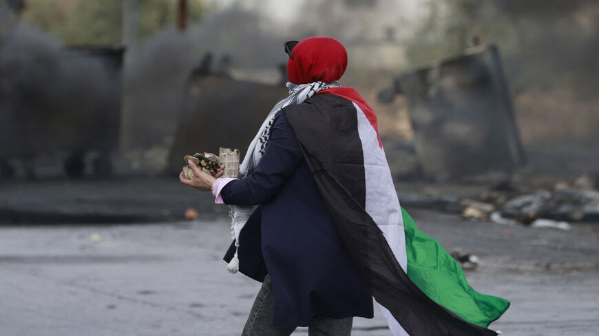 A woman draped in a Palestinian flag prepares to hurl stones toward Israeli forces during clashes with them at the northern entrance of the West Bank city of Ramallah near the Israeli settlement of Beit El on October 20, 2023, as battles continue between Israel and the Palestinian Hamas group. (Photo by Jaafar ASHTIYEH / AFP) (Photo by JAAFAR ASHTIYEH/AFP via Getty Images)