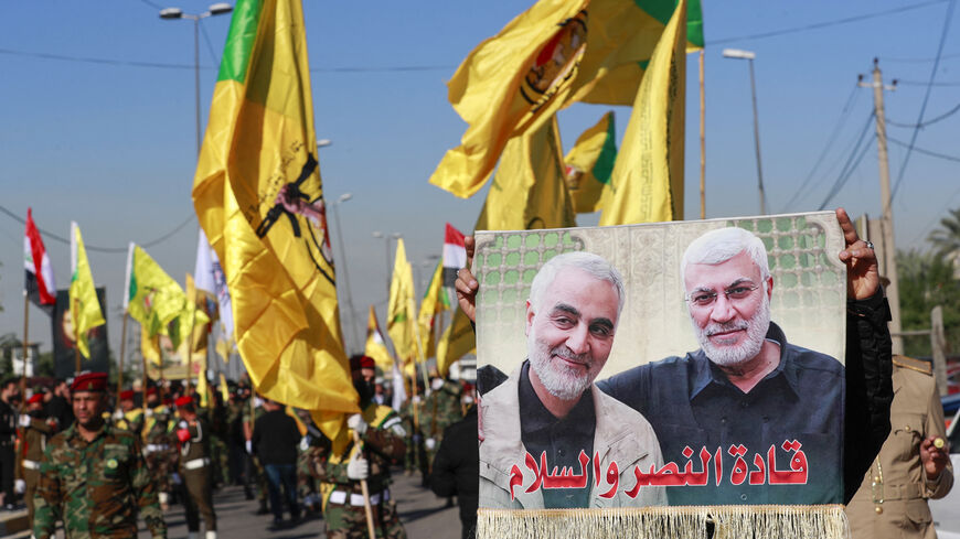 A man lifts a placard depicting slain Iranian commander Qasem Soleimani (L) and Iraqi commander Abu Mahdi al-Muhandis, as fighters bearing flags of Iraq and paramilitary groups, including al-Nujaba and Kataib Hezbollah, march during a funeral in Baghdad for five militants killed a day earlier in a US strike in northern Iraq, on December 4, 2023. Dozens of mourners gathered on December 4 for the funeral of the five militants killed the previous day near Kirkuk in what a US military official described as a "s