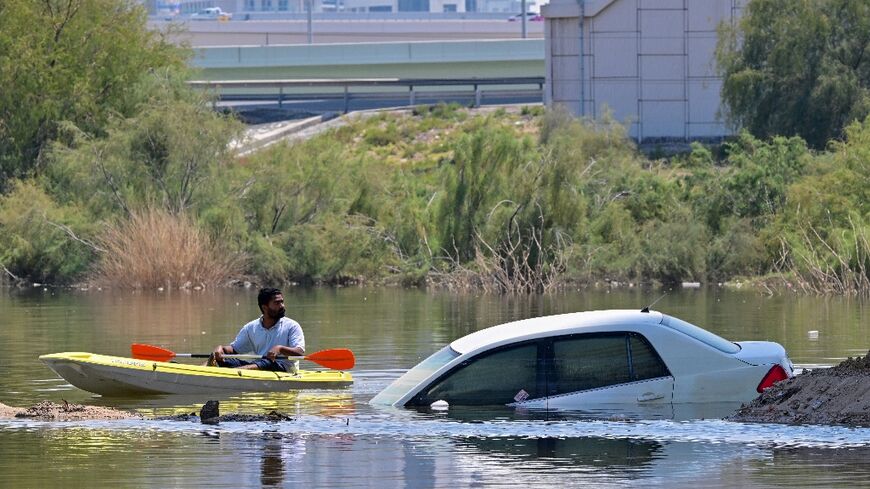 A man steers his canoe past a stranded car on a flooded street in Dubai