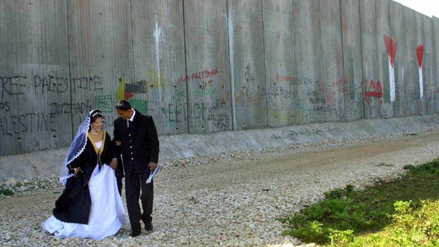 QALQILYA, -:  Palestinian bride Saja (L) and her groom Abdel Rahim Abu Aisha are photographed as they walk past the Israeli "security barrier" before taking their marriage vows in the West Bank town of Qalqilya 10 March 2004. Prime Minister Ariel Sharon paid a visit today to the controversial separation barrier being built by Israel around Jerusalem, his bureau said. Sharon was accompanied by regional military commander General Moshe Kaplinsky as well as his national security advisor Giora Eiland, the offic