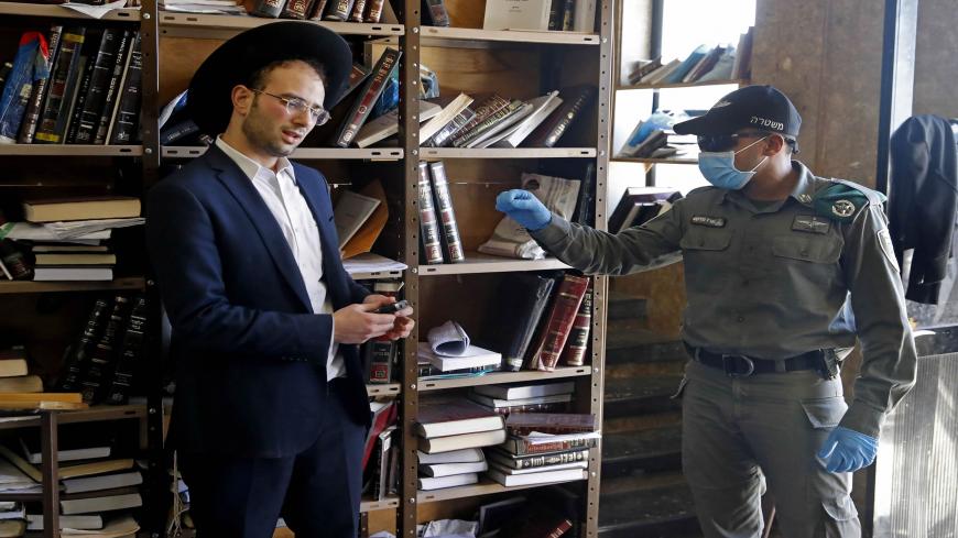 An Israeli police officer, dressed in protective outfit, speaks to a Yeshiva (Jewish educational institution for studies of traditional religious texts)student, in the Israeli city of Bnei Brak on April 2, 2020, during a control to insure that social distancing measures imposed by Israeli authorities meant to curb the spread of the novel coronavirus are being respected. (Photo by JACK GUEZ / AFP) (Photo by JACK GUEZ/AFP via Getty Images)