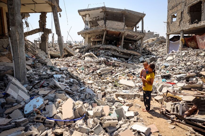 A woman holds a child amid the rubble of buildings destroyed during Israeli bombardment in Khan Yunis in the southern Gaza Strip on June 23, 2024