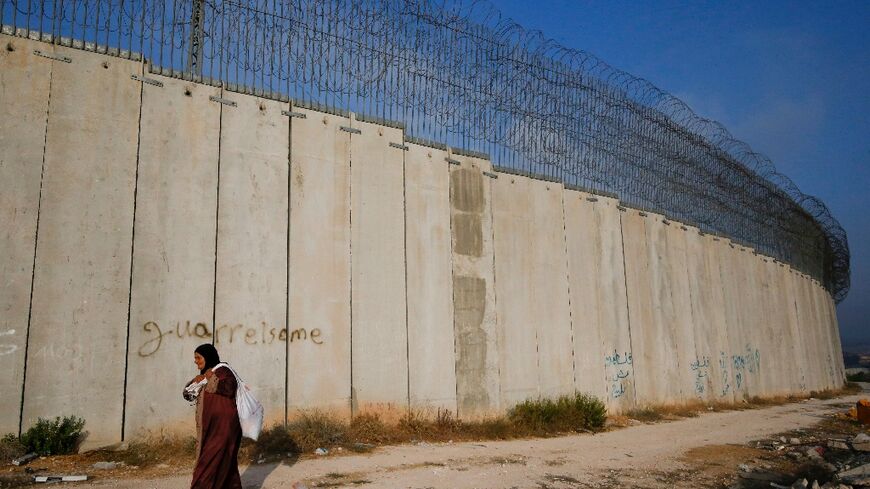 A Palestinian woman walks next to the Israeli separation barrier in the West Bank southwest of Hebron, in this October 10, 2020 photograph