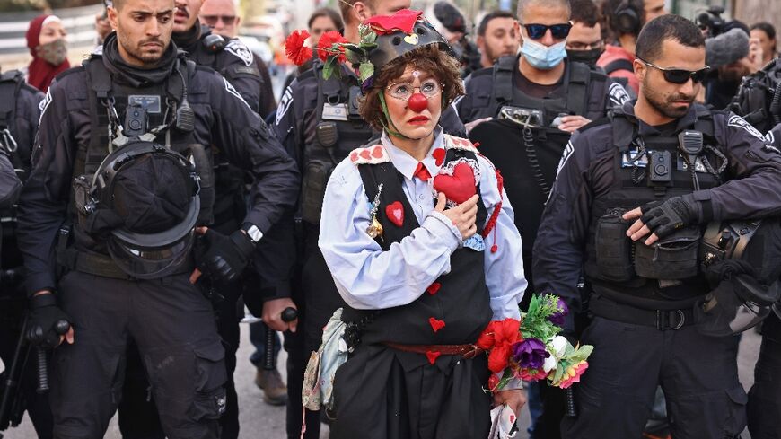 A protester dressed as a clown stands before Israeli police during a demonstration in the flashpoint neighbourhood of Sheikh Jarrah in Israeli-annexed east Jerusalem on February 18, 2022