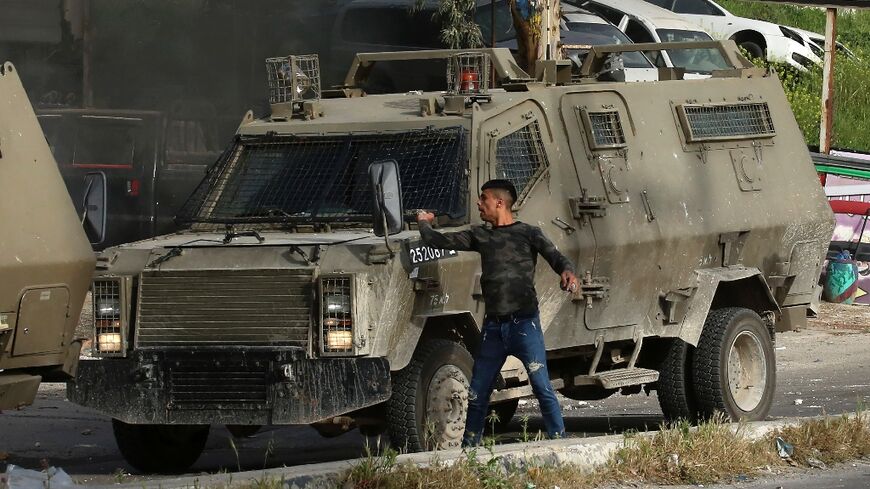 A Palestinian man hurls stones from behind an Israeli security armoured vehicle during a raid to look for wanted Palestinians in Nablus city, in the occupied West Bank