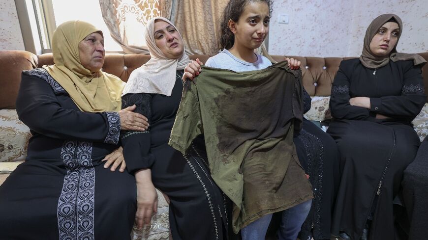 The sister of Palestinian Mohammed al-Shaham, 21, who was killed during an Israeli raid, holds his bloodied shirt, standing in front of their mother, who is seated second from left, and other relatives