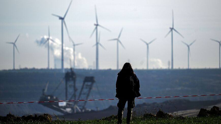 A woman stands on the edge of Germany's Garzweiler lignite open cast mine on November 12, 2022, with wind turbines in the background