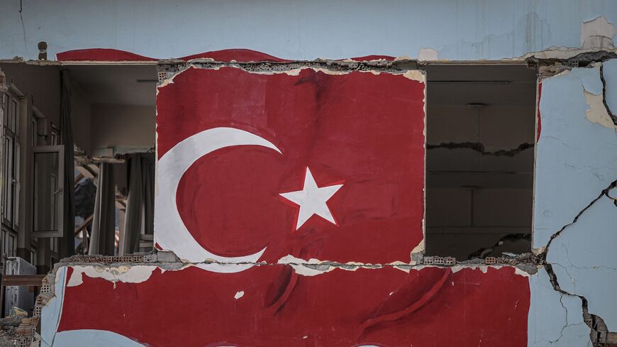 A painted Turkish national flag is seen on the wall of a collapsed building, two months after a 7.8-magnitude jolt and its aftershocks wiped out swathes of Turkey's mountainous southeast, in Antakya on April 5, 2023. - Many of the survivors blamed the government and its stuttering response to Turkey's worst disaster of its modern era for a death toll that has now surpassed 50,000. But that fury is gradually giving way to a mixture of fatalism and reviving trust in the man this province gave three-fourths of