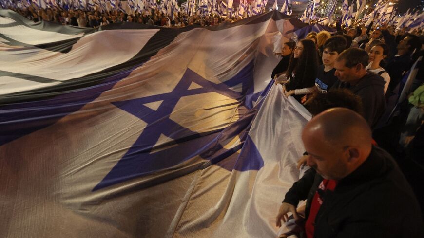 Demonstrators lift a large national flag during a rally to protest the Israeli government's judicial overhaul bill in Tel Aviv, on April 29, 2023