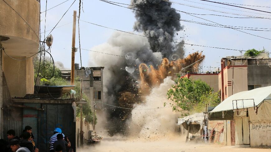 People take cover behind a wall as a building in Beit Lahia in the northern Gaza Strip is hit by an Israeli air strike on May 12