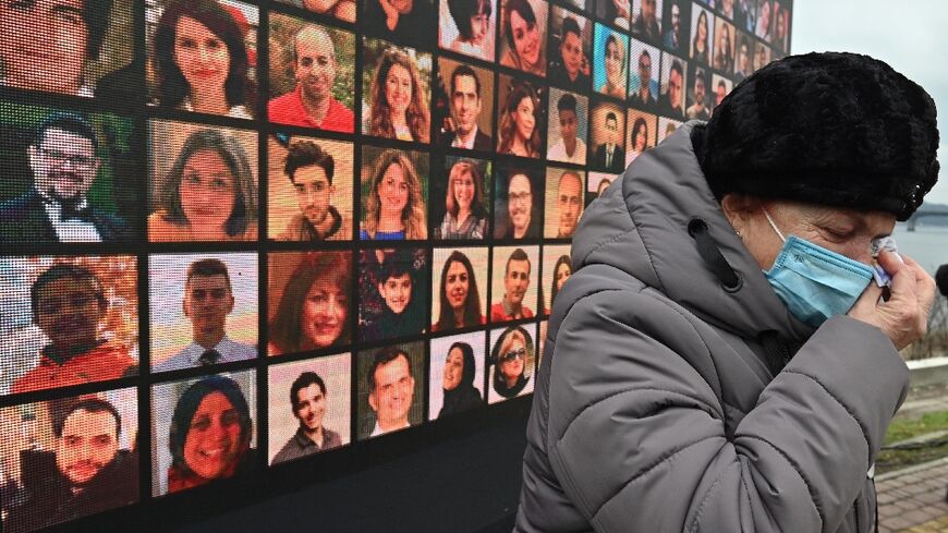 A woman cries in front of a huge screen bearing portraits of late crew members and passengers of Ukraine International Airlines Flight 752, during a commemorative ceremony on January 8, 2021 in Ukraine's capital Kiev