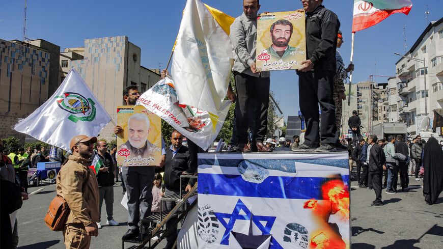 Men hold a sign showing the face of Ahmed Mutawasilian, a fighter in Iran's Islamic Revolutionary Guard Corps (IRGC) who was kidnapped and killed in Lebanon in 1981, as they stand upon a podium showing a picture of a burning Israeli flag defaced with footprints during a rally marking Al-Quds Day (Jerusalem), a commemorative day held annually on the last Friday of the Muslim fasting month of Ramadan by an initiative started by late Iranian revolutionary leader Ayatollah Ruhollah Khomeini, in Tehran on April 
