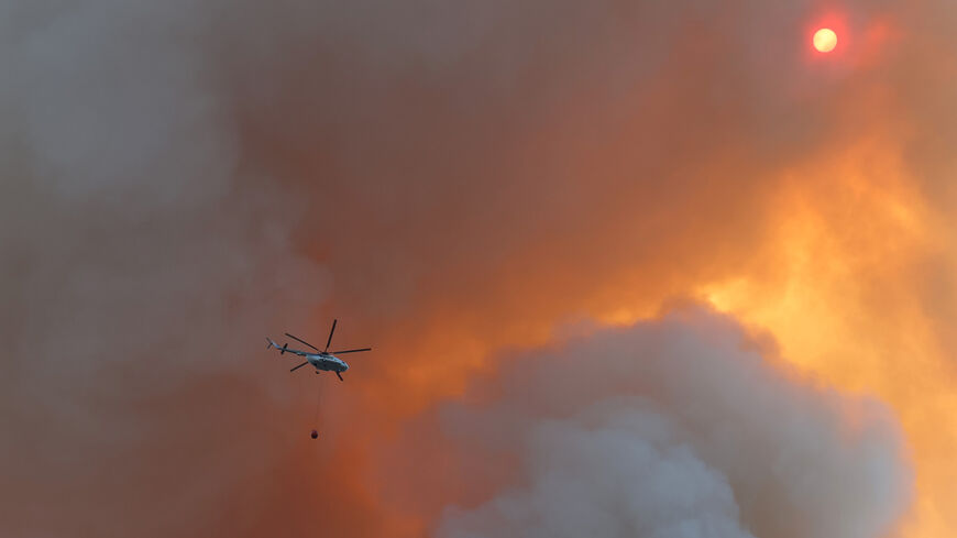This photograph taken on July 13, 2022, shows a firefighting helicopter carrying water over a wildfire.