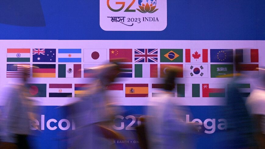 People walk past a banner with flags of countries participating in the G20 summit in New Delhi