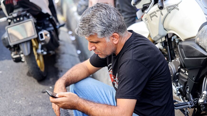 A man browses a phone while sitting next to a motorcycle along a street in Tehran on September 10, 2023. Iranian authorities have blocked popular social media networks, including Instagram and WhatsApp since mass protests erupted following the September 2022 death in police custody of 22-year-old Iranian Kurd Mahsa Amini. The restrictions come as millions of Iranians struggle to make ends meet, grappling with in an economic crisis marked by crippling Western sanctions, a galloping inflation, and sharp decli