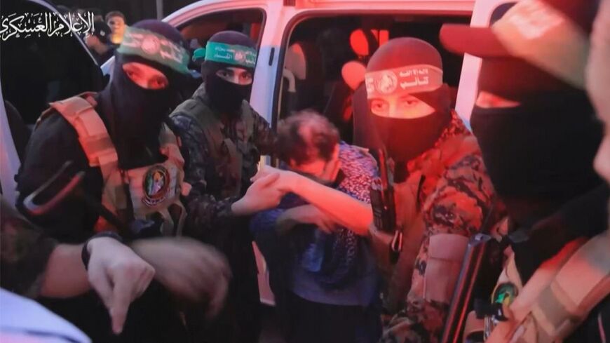 A member of Hamas' Al-Qassam Brigades helps a hostage out of a car before handing them over to officials from the International Committee of the Red Cross in Gaza