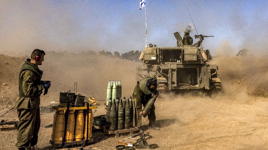An Israeli army soldier carries rounds from a stockpile towards a stationed self-propelled artillery howitzer firing from a position near the border with the Gaza Strip in southern Israel