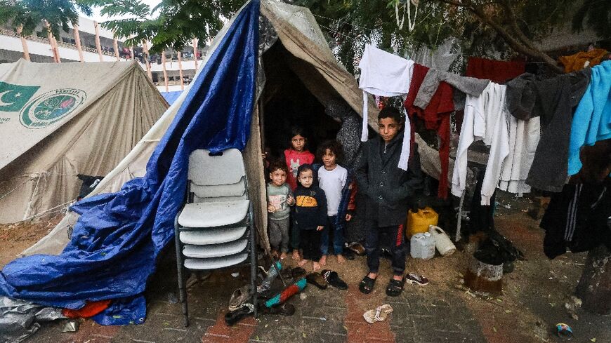 Palestinians children pose outside their makeshift tent at a camp set up in a schoolyard in Rafah in the southern Gaza Strip where most civilians have taken refuge, on December 13, 2023
