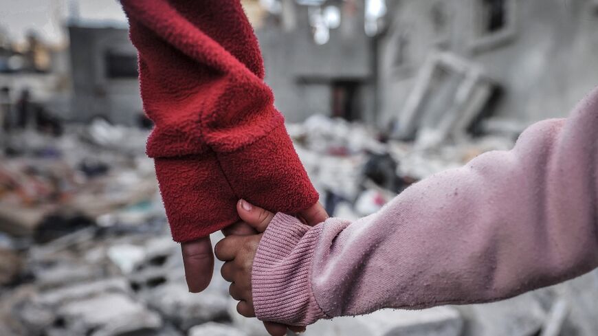 People hold hands as they inspect buildings hit during Israel's bombardment in Rafah in the southern Gaza Strip on December 29, 2023
