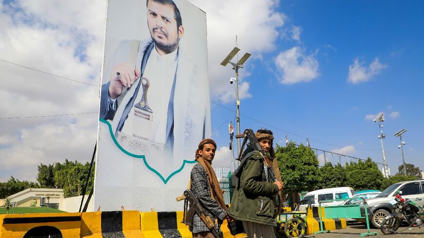 Yemeni fighters walk past a large portrait of Huthi leader Abdulmalik al-Huthi on a street in Sanaa on Thursday