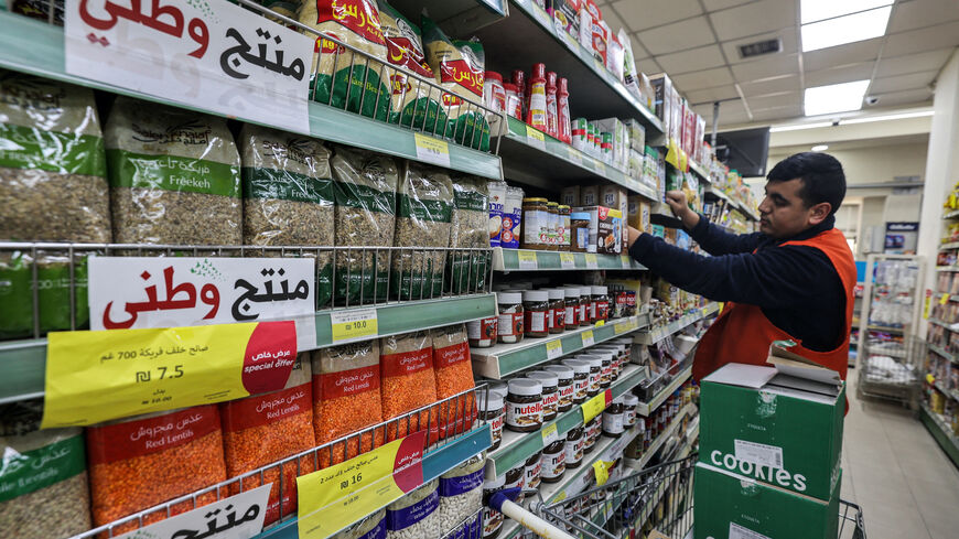 A worker arranges products on a shelf as nearby labels reading in Arabic "national product" are displayed on packaged items at a supermarket in Ramallah in the occupied West Bank on December 26, 2023, as part of a wider campaign urging Palestinians to boycott Israeli products and buy locally made goods. Since the war in Gaza began, a slew of boycott posters, stickers and leaflets has cropped up across the occupied West Bank. Many Palestinians are looking for alternatives as calls to ban Israeli goods also g