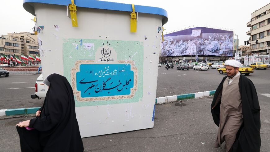 A Shiite Muslim cleric and a woman in front of an installation in the form of a giant ballot box, pictured  in Tehran on February 28, 2024, ahead of the elections