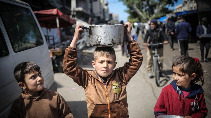 Children clutching pots and pans head for a food distribution point in Khan Yunis