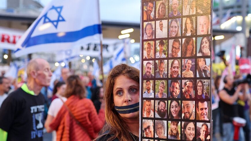 A protester with a zip over her mouth holds up photographs of the Israeli hostages at a Tel Aviv rally demanding that the government strike a deal with Hamas for their release