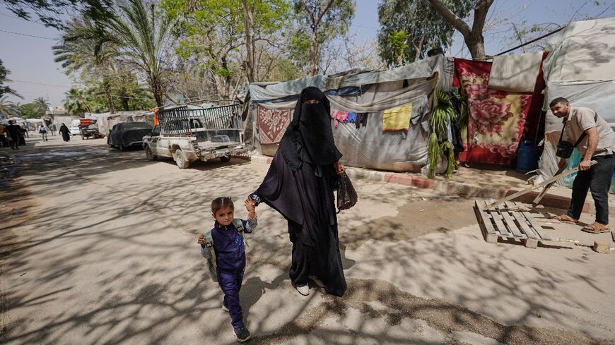 A displaced Palestinian woman holds a child by the hand as she walks in front of tents set up inside the European hospital compound in Khan Yunis in the southern Gaza Strip