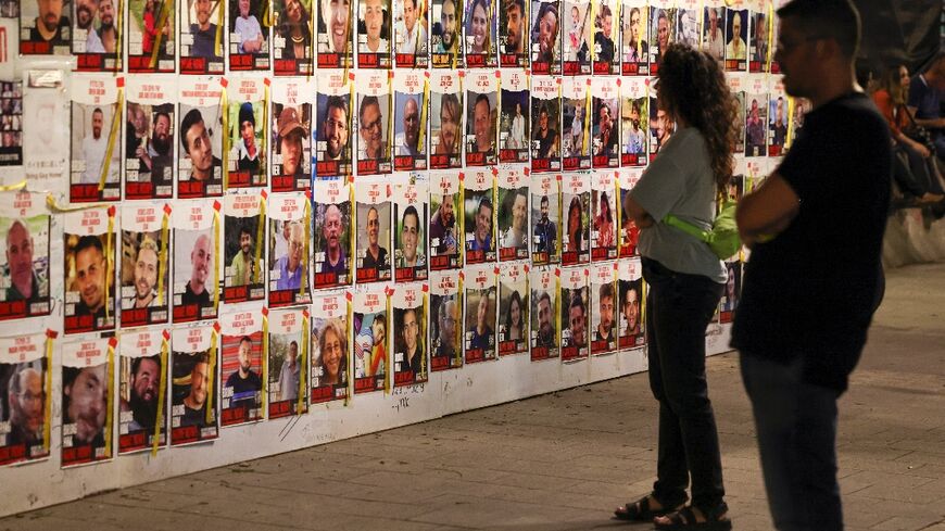 Israelis look at portraits of hostages, held in Gaza since the October 7 attack, posted on a wall in Tel Aviv