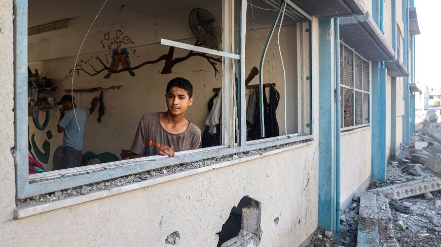 A Palestinian boy stands by a shattered window at a UN school sheltering displaced people which was damaged during Israeli bombardment in Khan Yunis, southern Gaza