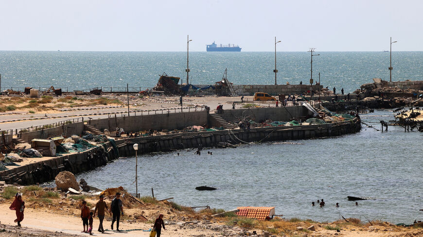 Palestinians walk past a jetty in Gaza City with a view of navy vessels off the coast as part of a humanitarian "maritime corridor" announced by US Central Command, amid the ongoing conflict in the Gaza Strip between Israel and Hamas, May 17, 2024.