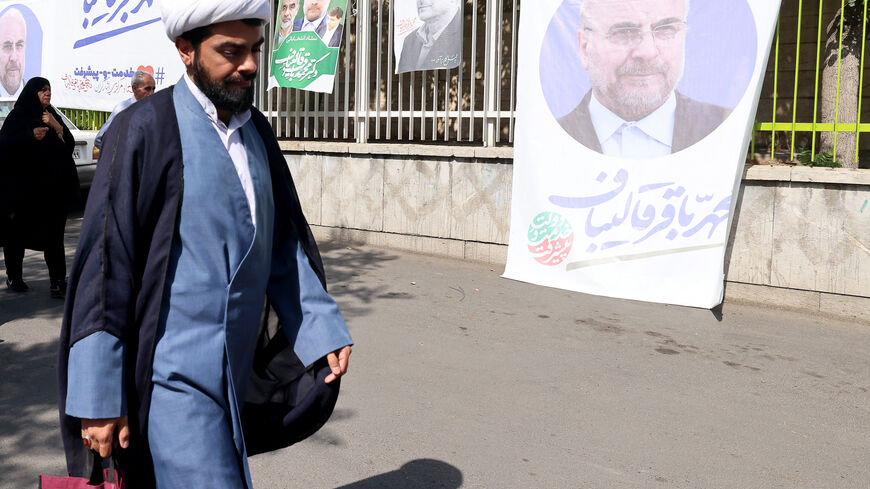 An Iranian cleric walks past a banner and posters with the image of presidential candidate, conservative Parliament Speaker Mohammad Bagher Ghalibaf, as he walks along a street days before the national snap elections, in Tehran on June 26, 2024. Six candidates are vying in the June 28 snap elections to succeed the ultraconservative president Ebrahim Raisi, who died in a helicopter crash on May 19, 2024. (Photo by ATTA KENARE / AFP) (Photo by ATTA KENARE/AFP via Getty Images)