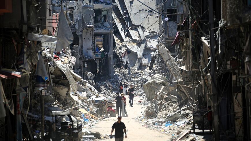 Palestinian men walk along a narrow street past destroyed buildings in Khan Yunis, in the southern Gaza Strip