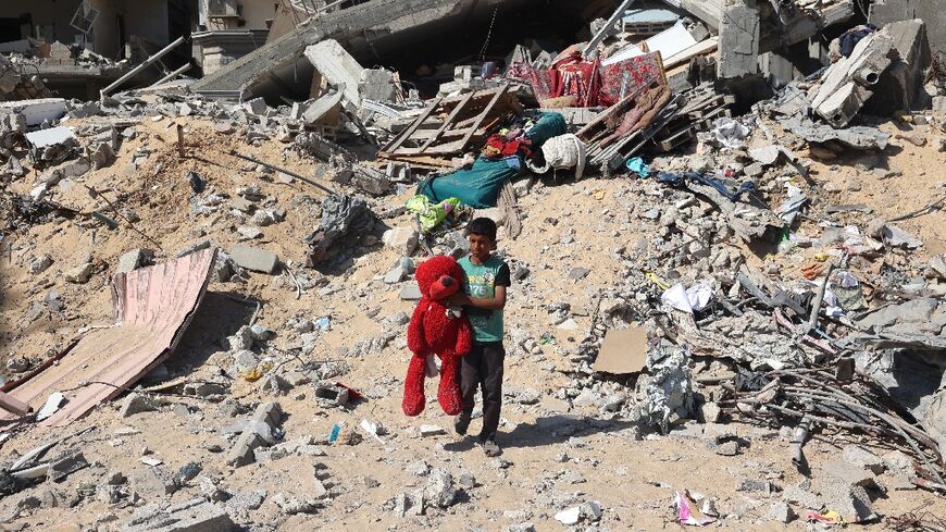 A Palestinian child walks with a toy bear recovered from the rubble of a destroyed building following Israeli bombardment in Khan Yunis, southern Gaza