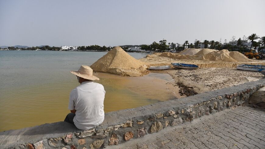 A man looks on as a digger spreads sand on a beach in the tourist town of Hammamet as authorities fight to protect the coast from rising sea levels and erosion