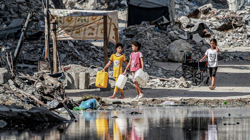 Girls walk with water containers past destroyed buildings and open sewage in Khan Yunis in the southern Gaza Strip on July 8, 2024 