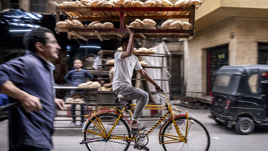 TOPSHOT - A deliveryman balances a tray of freshly baked bread while riding his bicycle along the al-Darb al-Ahmar district in the old quarters of Cairo on March 6, 2024. (Photo by Amir MAKAR / AFP) (Photo by AMIR MAKAR/AFP via Getty Images)