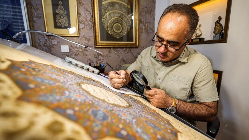 Mohammad Hossein Aghamiri, an artist who specialises in Persian miniatures, uses a magnifying glass as he works on one of his pieces depicting al-Fatiha, the first chapter of the Koran