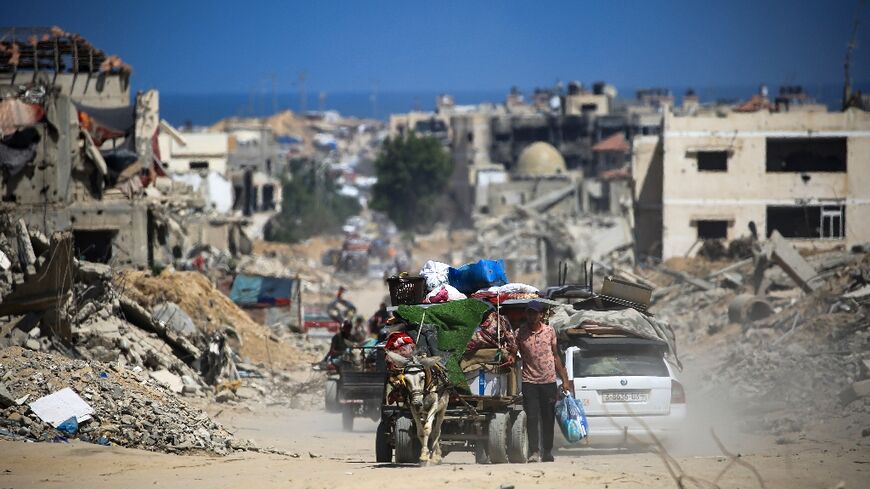 Palestinians walk and drive past buildings destroyed during previous Israeli bombardment in Khan Yunis in the southern Gaza Strip on July 3, 2024