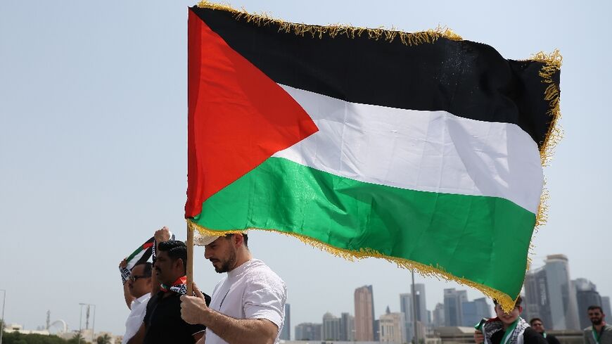 A man holds a Palestinian flag as he walks with others towards the Imam Muhammad bin Abdul Wahhab Mosque in Doha to bid farewell to slain Hamas leader Ismail Haniyeh after his killing in Iran in an attack blamed on Israel