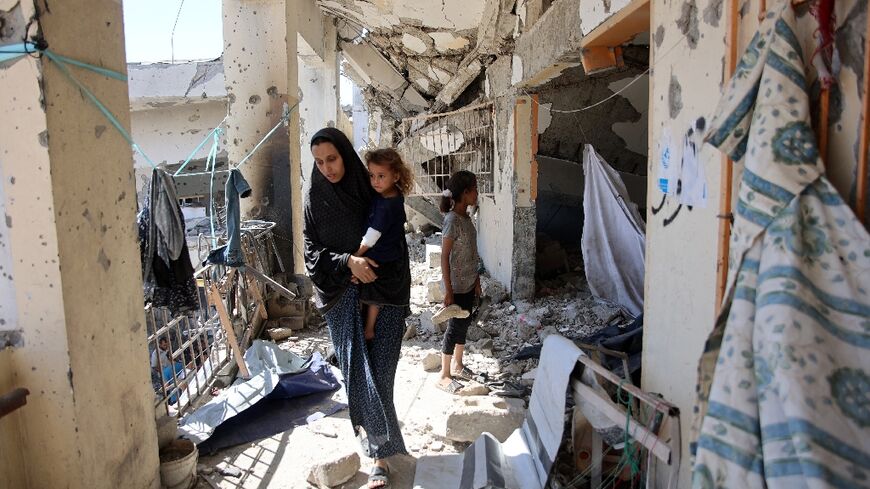 A Palestinian woman carrying a child checks the damage after a deadly Israeli strike on the Al-Zahra School in Gaza City where she and other displaced civilians had been sheltering