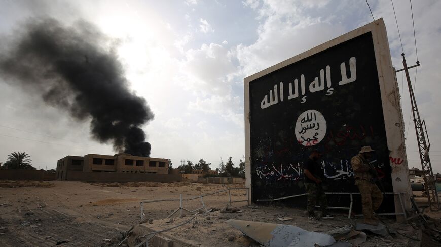 Iraqi fighters of the Hashed al-Shaabi stand next to a wall bearing the Islamic State (IS) group flag as they enter the city of Al Qaim as they fight against remnant pockets of Islamic State group jihadists on November 3, 2017. 