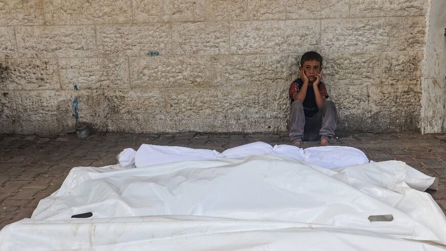 A child sits beside the shrouded corpses of people killed in an overnight Israeli strike, in the yard of the Al-Aqsa Martyrs hospital in Deir el-Balah in the central Gaza Strip