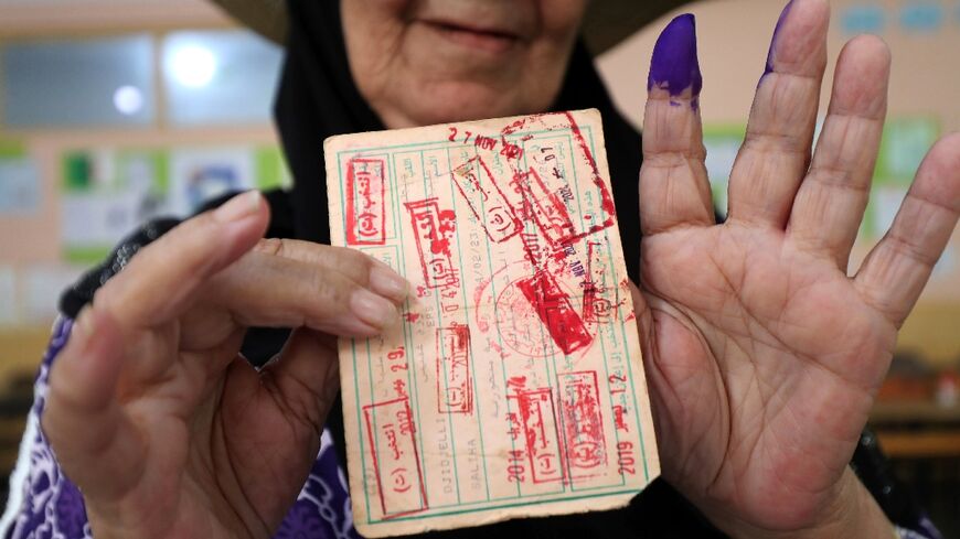 A voter displays her ink-stained finger and card after casting her ballot in Algiers