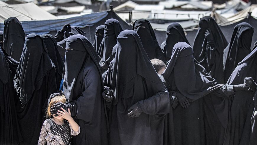 Women and a child queue to receive humanitarian aid packages at the Kurdish-run al-Hol camp.