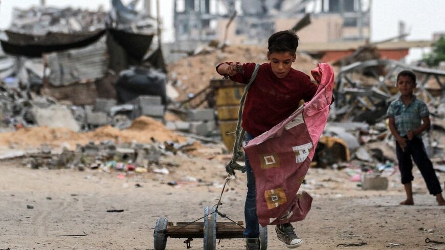 A boy pulls a cart with a rope while walking past a destroyed building in Khan Yunis in the southern Gaza Strip on October 7, 2024